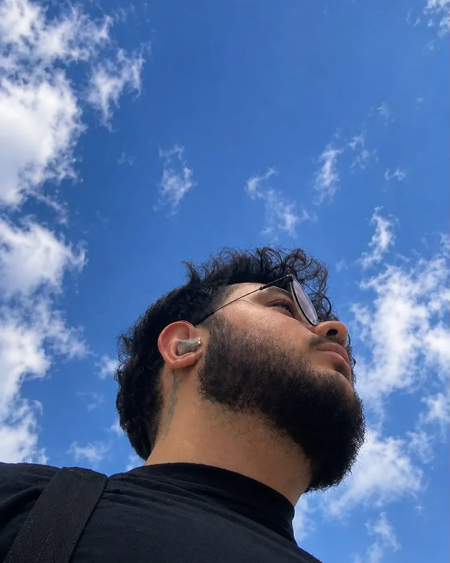 Arthur Reis, de baixo pra cima, contra um céu azul com nuvens